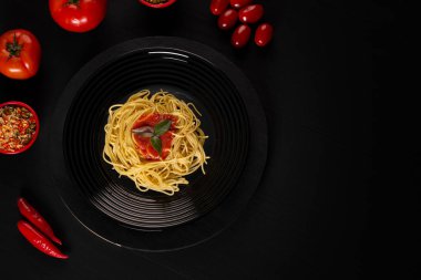 Spaghetti with sauce on a black plate in a darker studio photo.