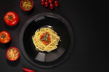 Spaghetti with sauce on a black plate in a darker studio photo.