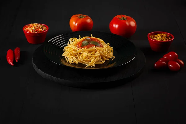 Spaghetti with sauce on a black plate in a darker studio photo.