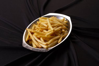 Masanın üstündeki gümüş kasede siyah kumaşlı patates kızartması.