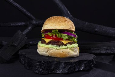 Siyah kumaşlı, ahşap kumaşlı, desenli ve siyah renkli bir masada dev bir hamburger.,