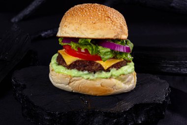 Siyah kumaşlı, ahşap kumaşlı, desenli ve siyah renkli bir masada dev bir hamburger.,