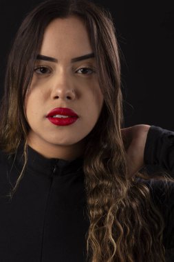 Siyah arka planda siyah elbiseler giyen kırmızı rujlu genç bir kadın.
