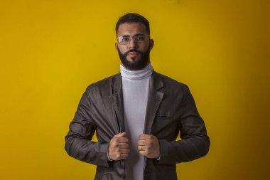 Gözlüklü, siyah deri ceketli, beyaz gömlekli, sakallı, değişik yüz ifadeli bir adam.