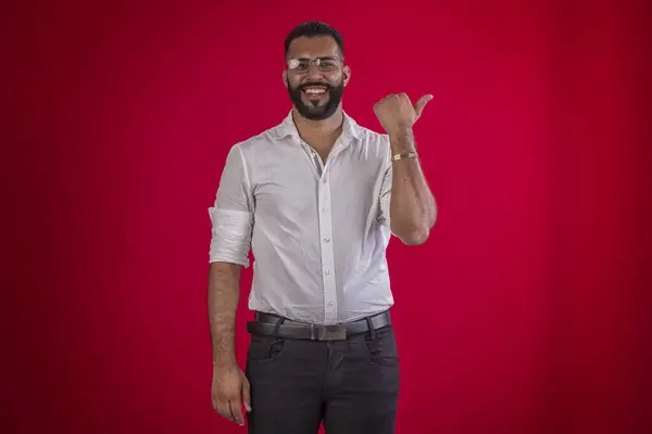 Adamım, sakallı, gözlüklü, beyaz gömlekli, değişik yüz ifadeli, kırmızı stüdyo arka planda.