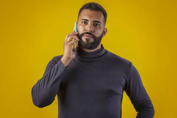 Sakallı, siyah tişörtlü, elinde cep telefonu olan, farklı yüz ifadeleri olan bir adam.