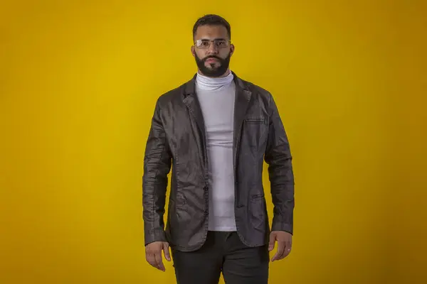 Gözlüklü, siyah deri ceketli, beyaz gömlekli, sakallı, değişik yüz ifadeli bir adam.