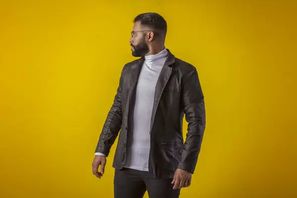 Gözlüklü, siyah deri ceketli, beyaz gömlekli, sakallı, değişik yüz ifadeli bir adam.