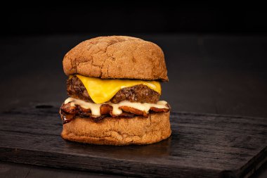 Kahverengi ve siyah odunlu bir stüdyo fotoğrafında patates kızartması ve soda eşliğinde hamburger.