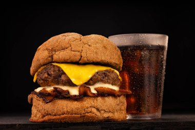 Kahverengi ve siyah odunlu bir stüdyo fotoğrafında patates kızartması ve soda eşliğinde hamburger.
