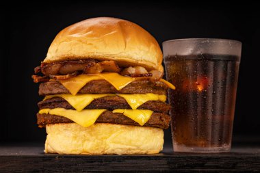 Kahverengi ve siyah odunlu bir stüdyo fotoğrafında patates kızartması ve soda eşliğinde hamburger.