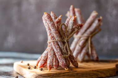 İtalyan sosisi. Tahtada fiyonklu lezzetli kuru sosis, siyah beton arka plan ve arkasında bir yığın kuru sosis, yakın plan..