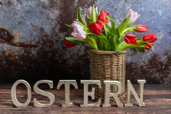Easter concept, rustic wooden letters form Easter lettering. In the background are colorful tulips in a vase made of willow branches, copy space.