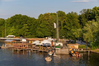 Berlin-Treptow, Almanya - 9 Haziran 2023, Treptower Park 'ta restoranları ve birkaç tekne kiralama ile Spree manzarası. Gezinti tekneleri nehre gider, uzayı taklit ederler..