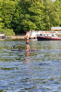 Berlin-Treptow, Almanya - 9 Haziran 2023, Spree Nehri 'nde ayakta kürek çeken genç adam. Yaz aktiviteleri ve su sporları. Kopyalamak için boşluk. seçici odak.