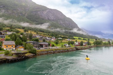 Olden, Norveç-18 Temmuz 2023 Olden 'in sisli kıyıları. Oldener Fjord 'da sakin bir köy, sabah sisi ile kaplanmış, resimli evler ve yemyeşil bitkilerle dolu. Su tarafından bak..