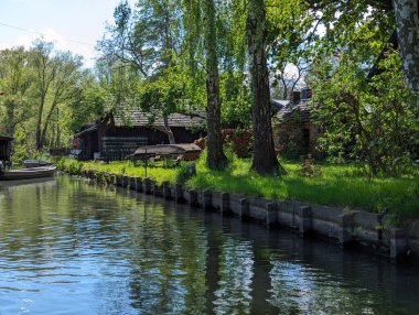 Almanya, Spreewald Biyosfer Rezervi, 27 Nisan 2024: Spreewald 'da canlı bahar yaprakları ve berrak suların arasına yerleşmiş geleneksel ahşap mimariyle sakin bir nehir kenarı..