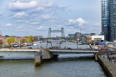 Rotterdam, Hollanda - 1 Nisan 2024: De Hef köprüsü ve Maas Nehri 'nden görünen binalar, köprünün altından geçen tekneler ve yaya geçitleri.