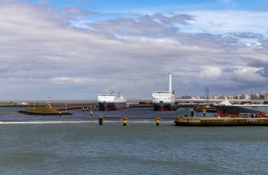 Zeebrugge, Belçika-2 Nisan 2024, iki büyük feribot ve birkaç kargo gemisi limana yanaştı. Vinçler, rıhtımlar ve uzak şehir manzarası parçalı bulutlu gökyüzünün altında görülebilir..