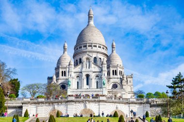 Paris, Fransa - 14 Nisan 2025: Sacre-Coeur Bazilikası 'nın beyaz kubbeleri mavi gökyüzünün altında yükselirken insanlar terasta toplanıyor..