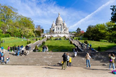 Paris, Fransa-14 Nisan 2025: Ziyaretçiler yeşil çimlerle çevrili Sacre-Coeur Bazilikası 'na ve açık bir gökyüzünün altındaki bahar ağaçlarına doğru merdivenlerden çıkıyorlar..