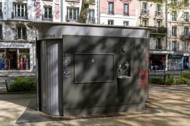 Paris, Fransa-14 Nisan 2025: Kamuya açık bir tuvalet gölgelerle ve bazı grafitilerle kaplıdır, arka planda dükkanlar ve yayalar vardır.