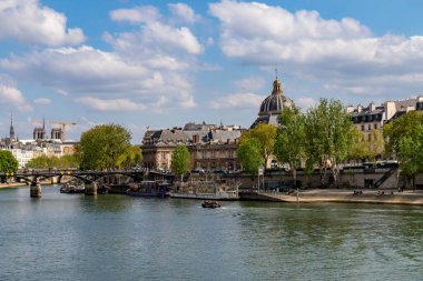 Paris, Fransa-14 Nisan 2025: Institut de France kubbesinin, ağaçların, teknelerin, tarihi nehir kıyısının ve Seine nehri kıyısındaki mavi yay altında binaların manzarası.