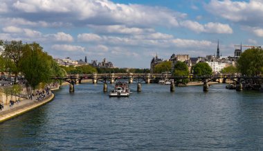 Paris, Fransa-14 Nisan 2025: Paris 'te tarihi Paris binaları tarafından çerçevelenen Pont des Arts köprüsü altında turistlerle dolu bir nehir teknesi denize açıldı.