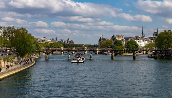 Paris, Fransa-14 Nisan 2025: Paris 'te tarihi Paris binaları tarafından çerçevelenen Pont des Arts köprüsü altında turistlerle dolu bir nehir teknesi denize açıldı.