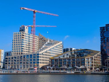 Aarhus, Danimarka-15 Ağustos 2025: Su kenarında uzun kırmızı vinçleri, açık gökyüzü ve liman faaliyetleri olan yerleşim yerleri.