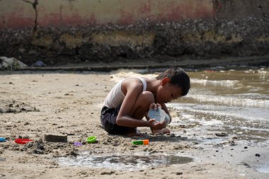 Jakarta, Indonesia on May 20,2024: Asian boys are playing in the sand on the edge of Ancol beach alone. defocused