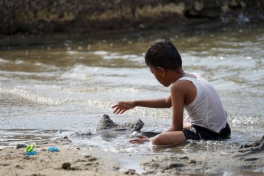 Jakarta, Indonesia on May 20,2024 : Asian boy is playing in the sand alone on the edge of Ancol beach. defocused