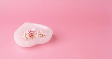 Kalp şeklinde beyaz kalsit plaka. Yumuşak pembe arka planda narin kayısı çiçekleri, fotokopi alanı stop-motion videosu var..