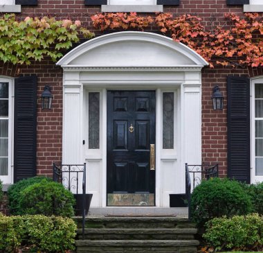 Kapısında sarmaşık ve kepenkleri olan iki katlı geleneksel tuğla ev.