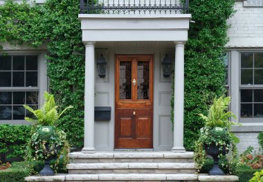 Portico girişi ve zarif ahşap ön kapısı olan sarmaşık kaplı bir ev.