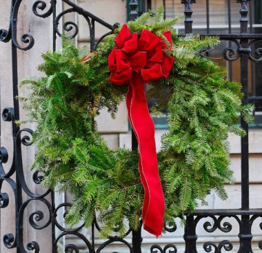 Dekoratif çam çelengi, dış metal kapısında parlak kırmızı bir fiyonk.