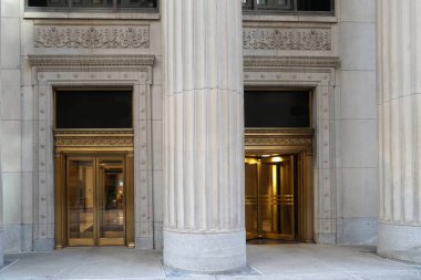 Büyük taş kolonlar ve döner kapılarla ofis binasına giriş.