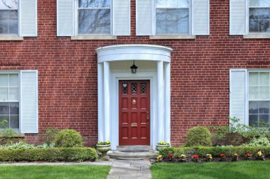 Beyaz panjurlu geleneksel iki katlı tuğla evin önünde.