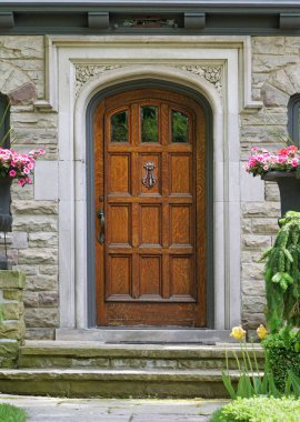 Taş evin ön kapısı ahşap renkli çiçeklerle dolu.