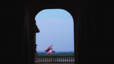 Tayland Bayrağı 'nın rüzgarda dalgalandığı sinematik bir video, karanlık tapınak binasından, geleneksel çitlerden, mavi gökyüzünden, nehirden ve arka plandaki yüksek kaliteli 4k' lık bir ormandan kaydedildi.