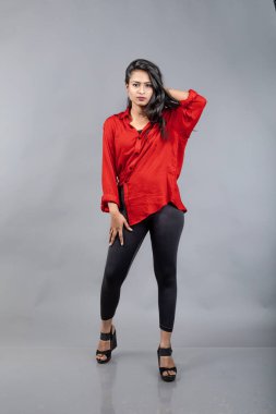 Gri arka plan karşısında gündelik giyimli Hintli genç bayan model - stok fotoğrafı. Kırmızı gömlek ve siyah kot giyen uzun siyah saçlı bir manken..