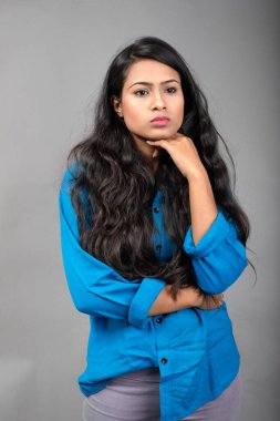 Gri arka plan karşısında gündelik giyimli Hintli genç manken. Stok fotoğrafı. Uzun siyah saç modeli mavi gömlek giyiyor..