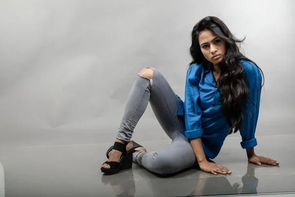 Indian female young model in casual wear against grey background - stock photo. Long black hair model wearing blue shirt, grey jeans and black heels.