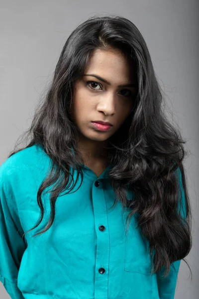 Indian female young model in casual wear against grey background - stock photo. Long black hair model wearing blue shirt.