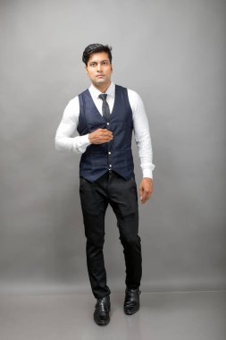Gri arka planda resmi giyinmiş neşeli, genç ve yakışıklı Hintli iş adamının stüdyo çekimi. Erkek model. Moda Portresi.