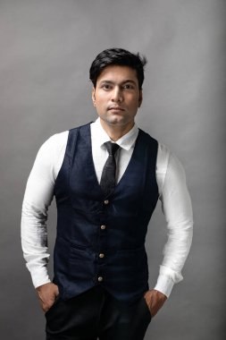 Gri arka planda resmi giyinmiş neşeli, genç ve yakışıklı Hintli iş adamının stüdyo çekimi. Erkek model. Moda Portresi.