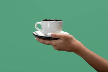 Beyaz çay fincanı ya da kahve fincanı ve tabağı yeşil arka planda tutan kadın.