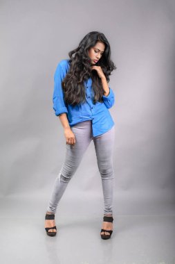 Gri arka plan karşısında gündelik giyimli Hintli genç manken. Stok fotoğrafı. Uzun siyah saç modeli mavi gömlek giyiyor..