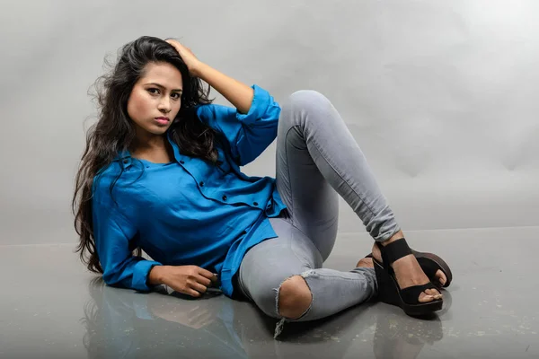 Indian female young model in casual wear against grey background - stock photo. Long black hair model wearing blue shirt, grey jeans and black heels.