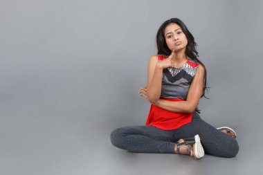 Gri arka planda kırmızı ve gri renkli ve mavi kot pantolon giyen, gündelik giyimli genç ve güzel bir Hintli kadın modelin stüdyo fotoğrafı. Kadın manken. Moda Portresi.